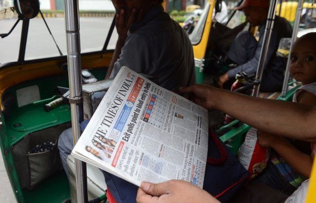 A commuter in an auto-rickshaw holds up a copy of an English-language Indian newspaper, with the headlines on exit polls