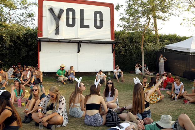 Crowds at Coachella festival 2014 sit near a sign modified to say "Yolo"