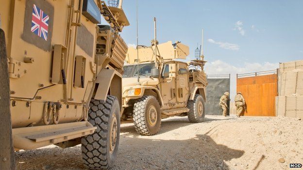 Two armoured vehicles leaving or entering a base as a soldier closes the gates in the background