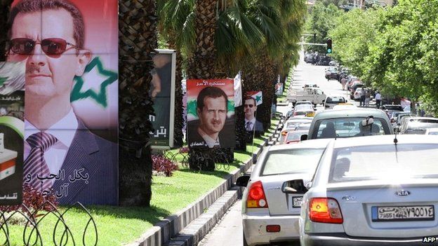 Syrians drive past election campaign posters bearing portraits of President Bashar al-Assad in Damascus - 18 May 2014