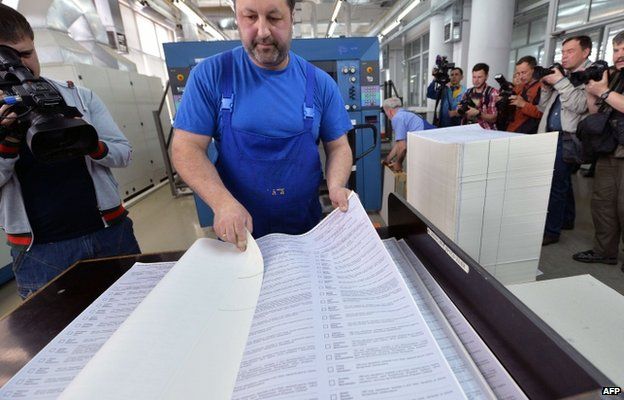 Photojournalists and cameramen film a worker examining ballots which will be use in early presidential election on May 25, during the printing process in printing house in Kiev on May 14, 2014.