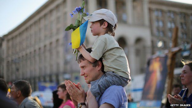 A young boy holds a flower and a Ukrainian flag as a "flash mob" sing traditional Ukrainian songs and pray for a peaceful election, in Kiev on 24 May 2014