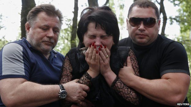 A grieving woman is being supported by two men near the coffin of a taxi driver shot in clashes near Donetsk airport (29 May 2014)