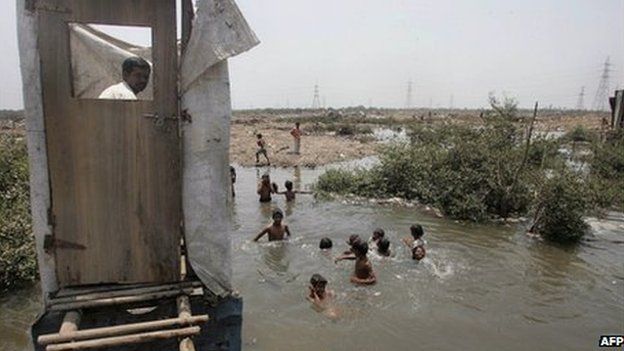 This May 12, 2006 file photograph shows a slum resident (L) as he uses a toilet that opens into the water below as children swim in the water near a protest rally against the government for demolishing make-shift huts at Mandala in Mankhurd in north central Mumbai.