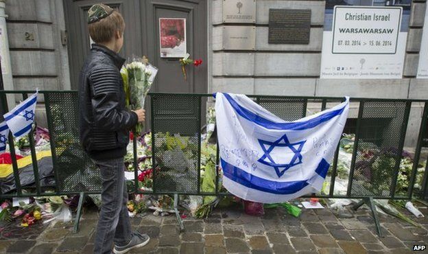 A Jewish boy stands with flowers in front of an Israeli flag and flowers laid in front of the Jewish Museum in Brussels on 26 May 2014
