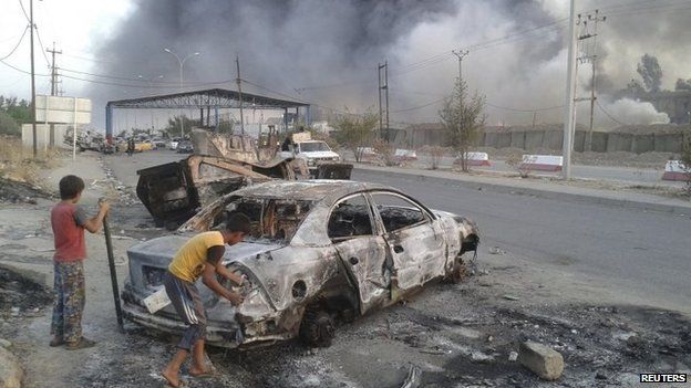Children stand next to a burnt vehicle during clashes between Iraqi security forces and ISIS