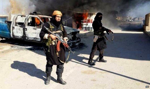 Undated image posted on a militant website in January 2014 shows Islamic State of Iraq and the Levant fighters next to a burning vehicle in Iraq's Anbar Province