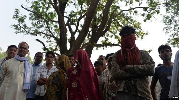 In this May 31, 2014, photo mothers of gang-rape victims (C, shawls covering their faces) and villagers stand in front of the mango tree where the girls were hanged in Katra Shahadatgunj in Badaun district