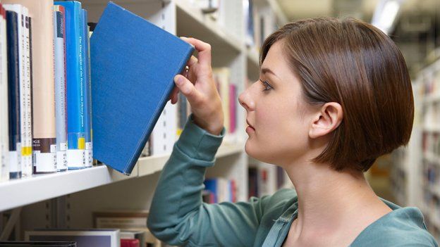 Woman takes book out of stack in library shelf