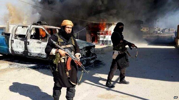 ISIS militants stand in front of a burning truck in Iraq.