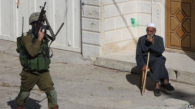 An Israeli soldier walks past a Palestinian man sitting on a street in the West Bank town of Hebron