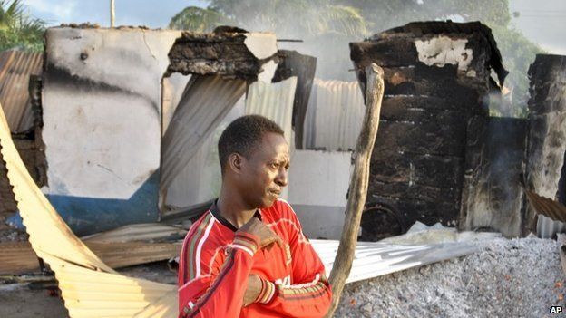 A man stands in front of the still-smouldering shell of a building set on fire by militants in the town of Mpeketoni on the coast of Kenya on 16 June 2014