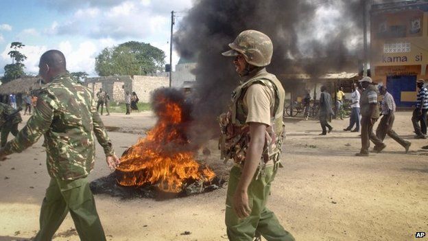 Armed security forces walk past a barricade of burning tyres set up by residents to protest against the recent killings and what they claimed was the government"s failure to provide them with enough security, in the village of Kibaoni just outside the town of Mpeketoni, about 60 miles (100 kilometers) from the Somali border on the coast of Kenya Tuesday, June 17, 2014.