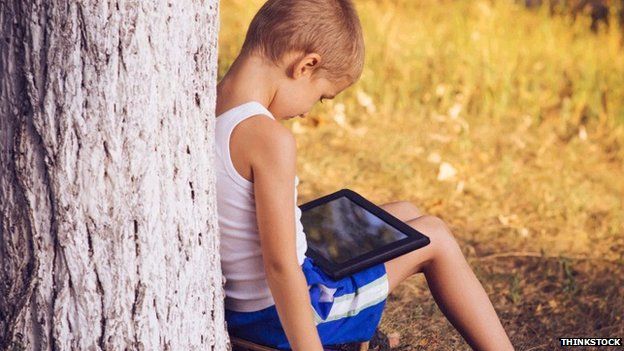 Boy using a tablet, lent against a tree