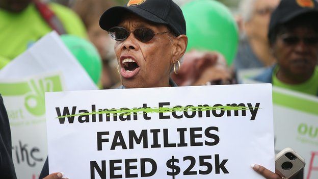 A woman holds up a sign at an anti-Walmart protest.