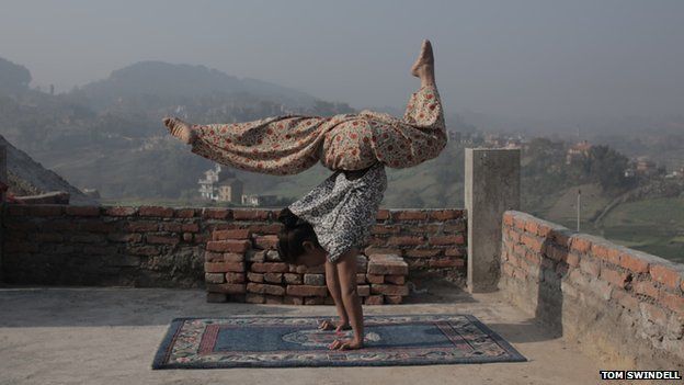 Circus performer stands on hands on rooftop overlooking mountains