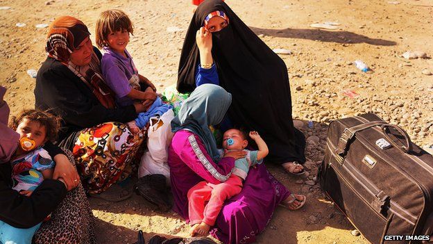 Iraqi families wait outside of a displacement camp for those caught-up in the fighting in and around the city of Mosul on June 28