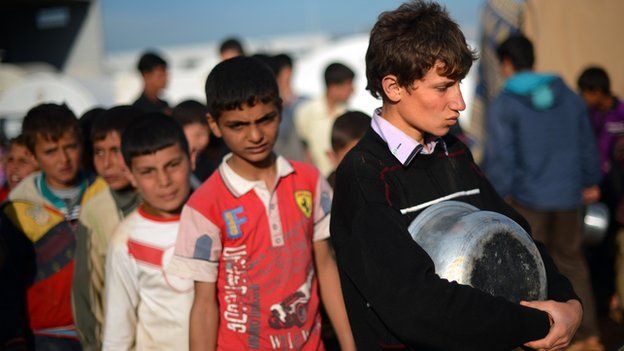 Internally displaced Syrian youths hold empty pots as they line up for food distribution