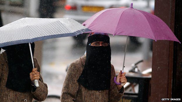 Women, sheltering under umbrellas, wear full face Niqab on the streets of Blackburn on 20 July 2010.