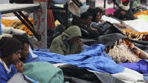 Eritrean migrants rest under blankets in the courtyard at a food distribution centre after they fled their makeshift camp to find shelter in Calais (May 2014)