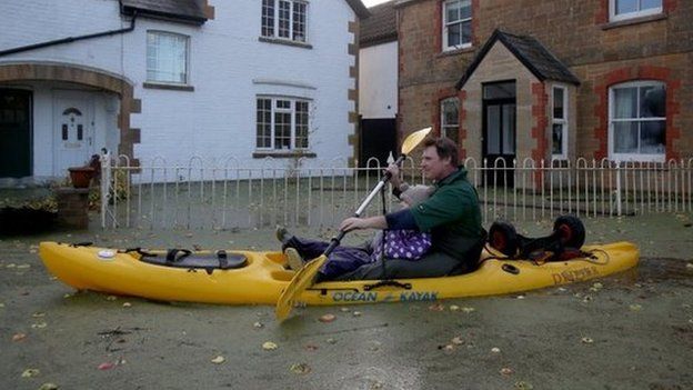 A resident uses a canoe on flood water past houses on the road leading to Muchelney
