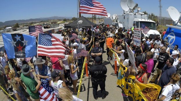 Demonstrators from opposing sides confront each other while being separated by Murrieta police officers, outside a US Border Patrol station in Murrieta, California 4 July 2014