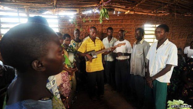 A man plays a guitar made out of wood and a empty can of oil while leading others in song during a prayer service at a church in Mutambara, Burundi - 2010