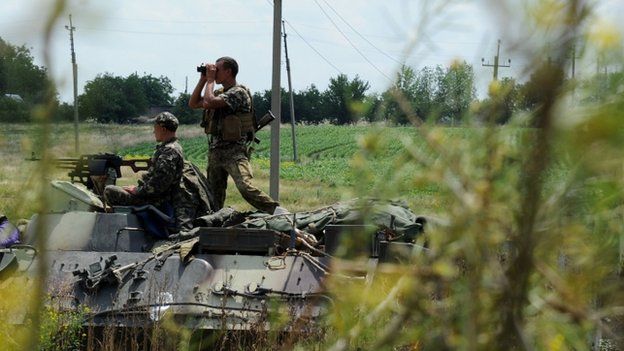 A Ukrainian government soldier looks though binoculars from the top of an armoured vehicle as Ukrainian troops take up a position some 20km south of Donetsk, eastern Ukraine on 10 July 2014