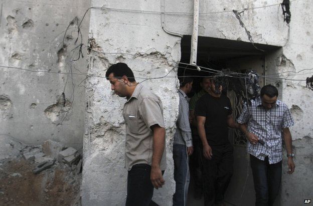 Palestinians pass a damaged house after a Palestinian rocket hit Hebron in the West Bank, 12 July