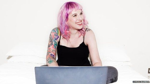 Kat Williams, blogger with pink hair and tattoos sits at her laptop