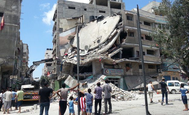 People in Gaza City look at a building destroyed by an Israeli air strike, 19 July 2014