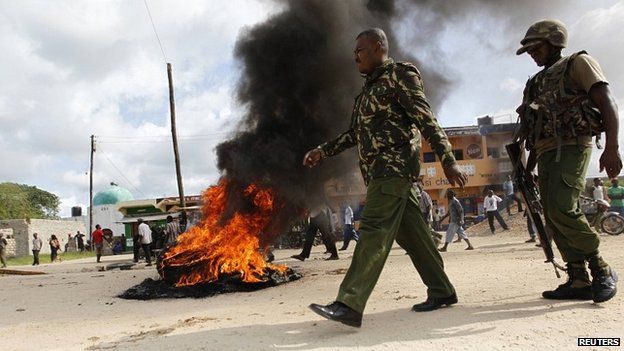 Kenyan police officers walk past a fire on a street in Mpeketoni after an attack by gunmen - 17 June 2014