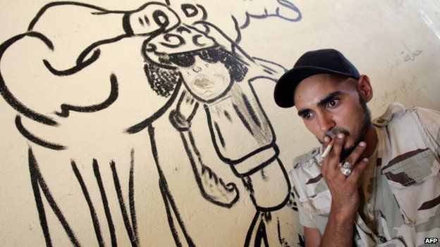A Libyan fighter smokes a cigarette next to graffiti depicting slain Libyan leader Muammar Gaddafi in the coastal city of Benghazi in October 2012