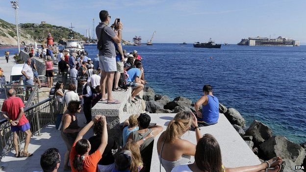 Locals and tourists watch the wrecked Italian cruise liner the Costa Concordia begin its final journey to the port of Genoa (23 July 2014)