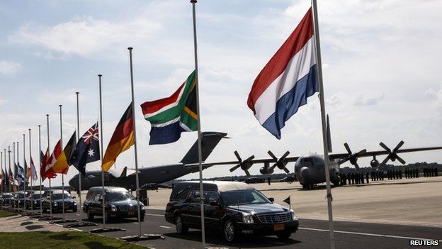 A convoy of hearses drive past international flags, flown at half-mast, as it leaves Eindhoven airport, to a military base in Hilversum, on 24 July 2014.