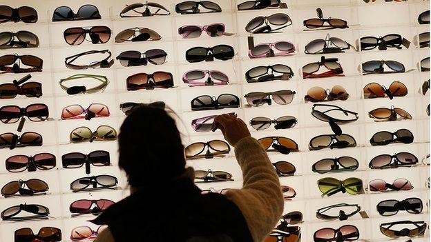 A women stands in front of a large display of sunglasses
