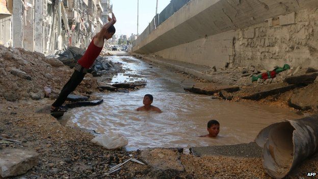Children playing in a flooded bomb crater in Aleppo (15 July 2014)