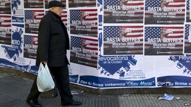 A man passes posters on a wall against the "vulture funds" in Buenos Aires, 18 June 2014