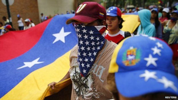 An anti-government protester covers his face with a US flag during a protest march in Caracas on 10 May, 2014