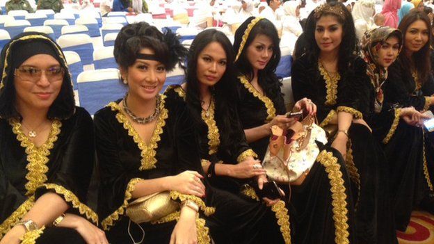 Beautifully dressed ladies sitting in a line at a social event