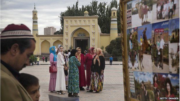 An Uighur man and his son look at photos as women stand in front of the Id Kah Mosque, China's largest mosque, on 31 July 2014 in Kashgar, Xinjiang Province, China.