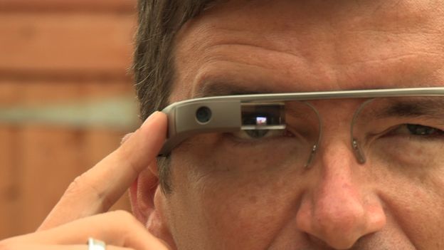 A close up of William wearing the Google Glass. The glass screen goes directly across his eye and his is pressing a button at the side of the glass
