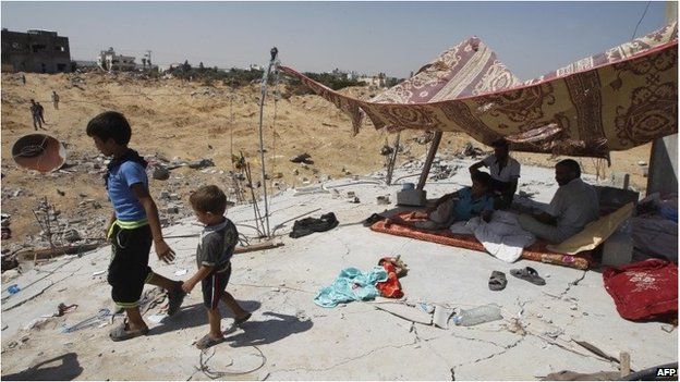 Children walk away from a makeshift shelter in Gaza. Adults are sitting under the shelter