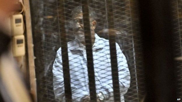 Egypt's ousted President Mohammed Morsi stands inside a glassed-in defendant's cage (28 January 2014)