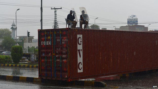 Pakistani policemen use their shields to protect themselves from rainfall as they sit on a container outside the house of the Pakistan Awami Tehreek (PAT) political party leader, Canadian-based cleric Tahir-ul-Qadri, in Lahore on August 9,