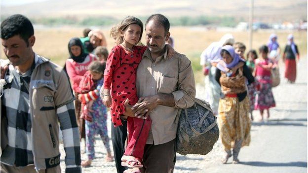 A displaced Iraqi man from the Yazidi community carries his daughter as they cross the Iraqi-Syrian border (11/08/2014)