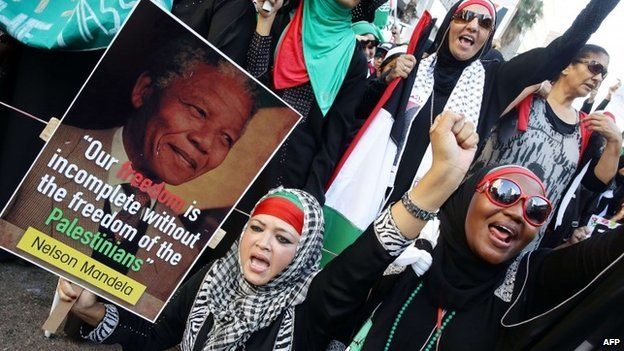 Women gestures while one holds a picture of late former South African president Nelson Mandela as they march through the streets of Durban following Friday prayer on 25 July 2014