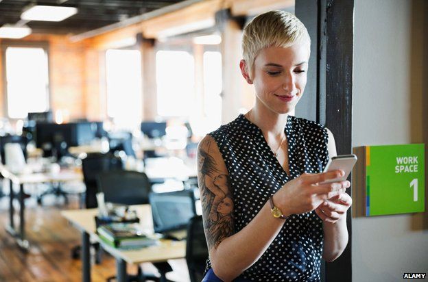 A woman on her phone in an office with a large tattoo on her upper arm