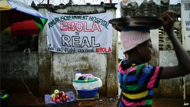 A girl walks past a sign warning of the dangers of Ebola outside a government hospital in Freetown on 13 August 2014