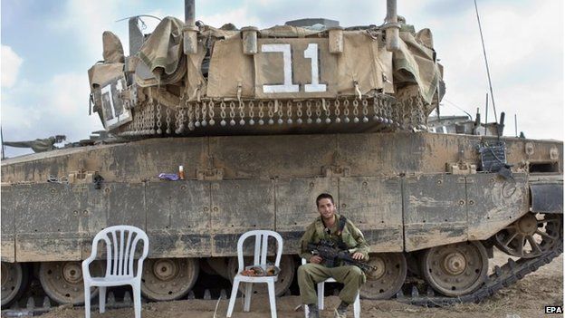 An Israeli soldier sits next to a Merkava tank in a staging area in southern Israel